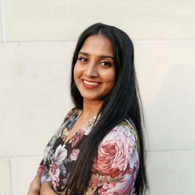 Photo of Dr Swathi Weaver,  woman with long black hair wearing a colorful floral shirt stands smiling against a neutral background.
