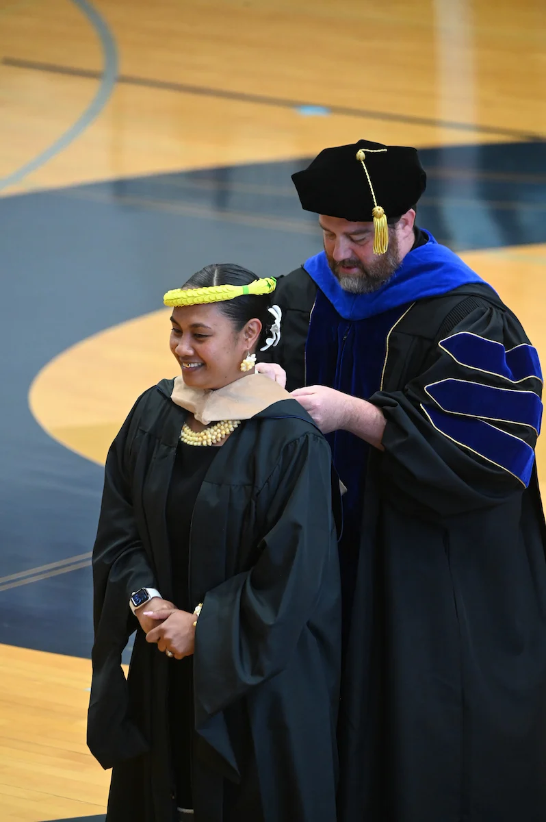 Professor Michael Fields hoods a Graduate at the College of Business commencement ceremony