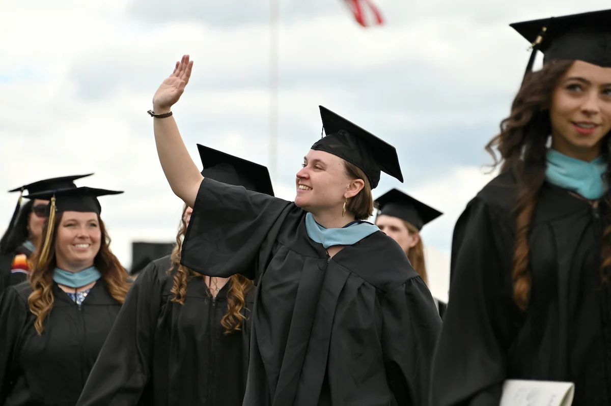 A Master of Education Graduate waves to the crowd on Commencement Day