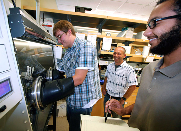 EOU student Jeremy Bard, left, manipulates protein samples inside an airtight “glove box." Fellow student Stone Safaie, right, takes notes while Colin Andrew, professor of chemistry, observes. The National Science Foundation is funding their ongoing research.