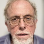 head shot of older male with light colored beard and glasses wearing blue shirt