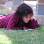 A student laying in the grass reading