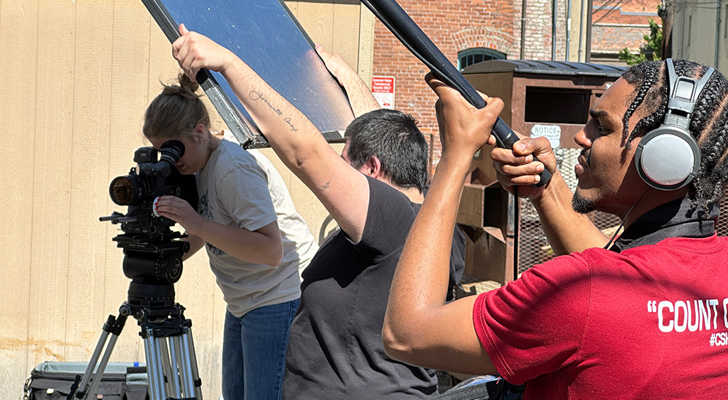 Quincy records the clearest audio for post-production while Abel keeps direct sunlight from flaring the lens.
