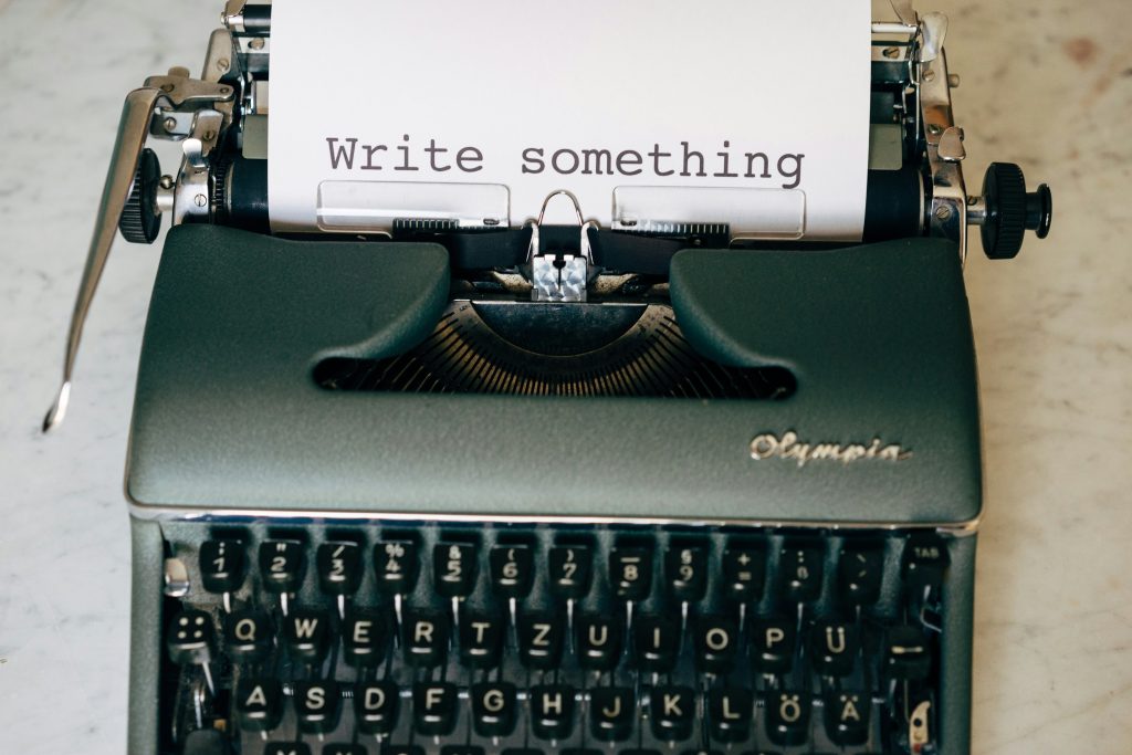 Close-up of a vintage Olympia typewriter with a sheet of paper that reads “Write something.”