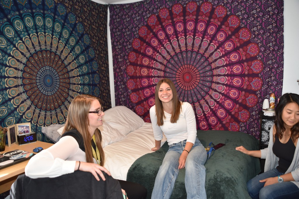 Three students sitting in a decorated Eocene bedroom smiling