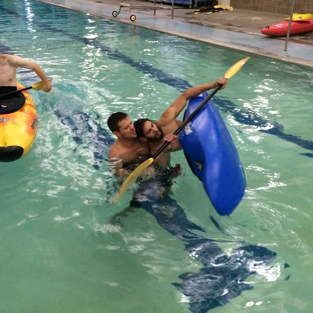 An instructor helps an OUT 180 Beginning Kayaking student learn how to roll the kayak at the local pool. 