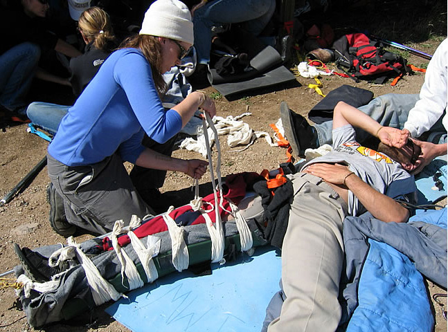 Photo shows a women creating a split for a leg fracture and representative of skills learned in OUT 352 Wilderness First Responder course.