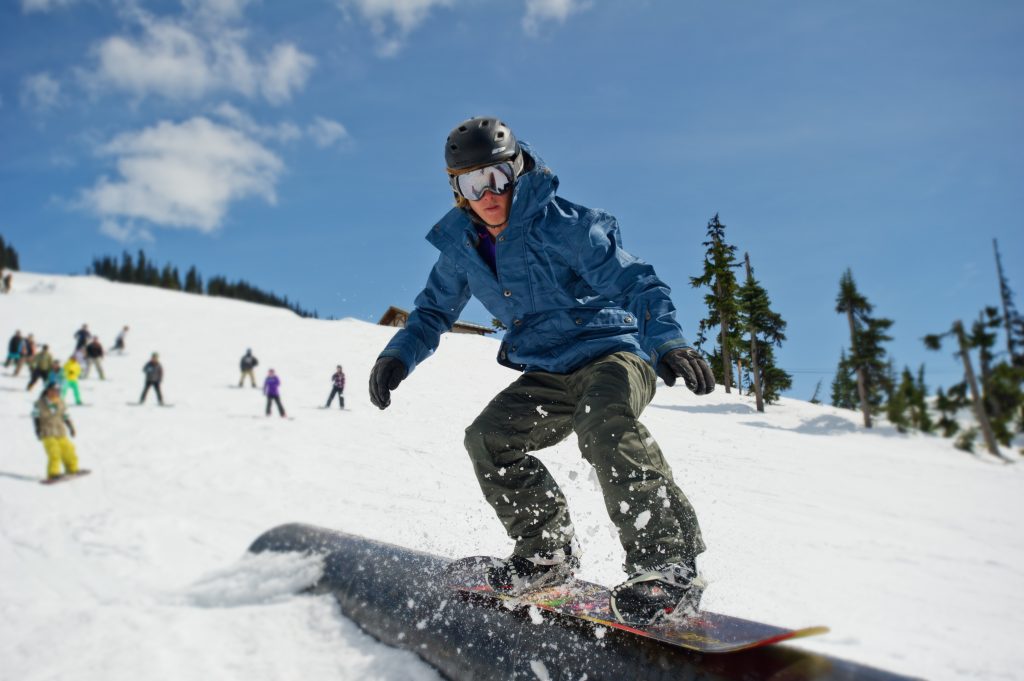 A snowboarder riding a rail and representative of skills learned in OUT 180 Advanced Snowboarding course. 