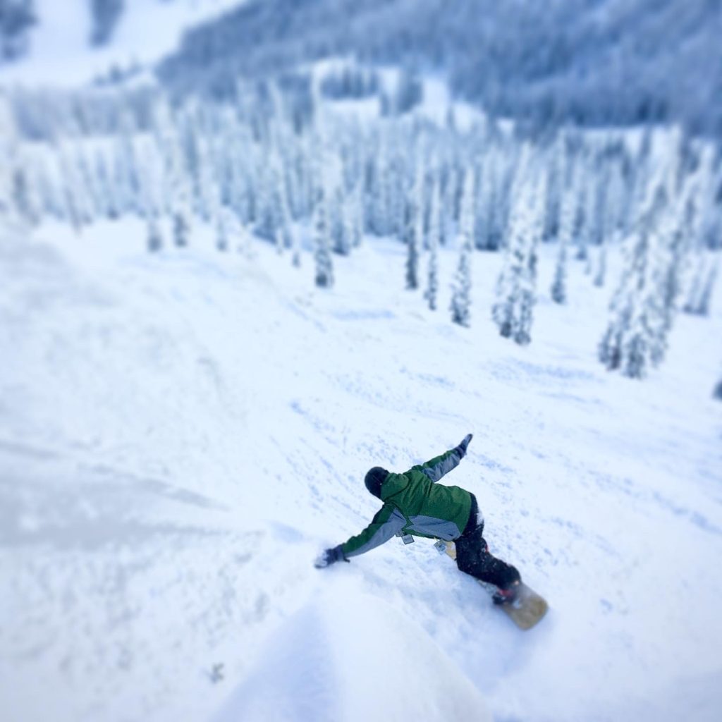 A snowboarder carving turns on the slopes and representative of skills learned when taking the OUT 180 Beginning Snowboarding course. 