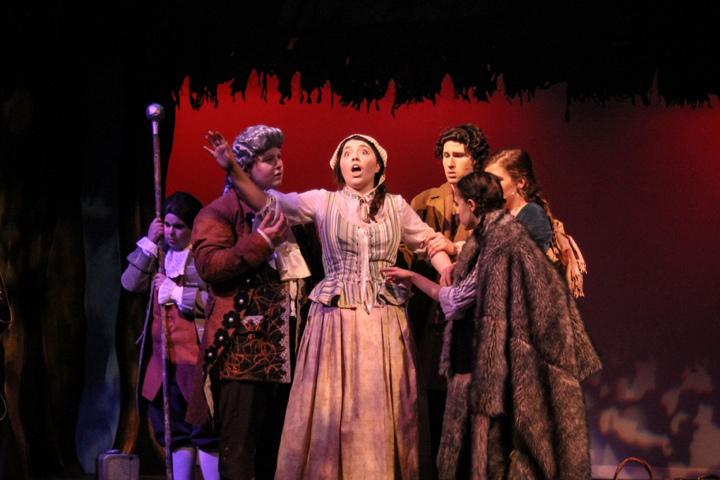 A group of students in costume standing around a singing girl on stage