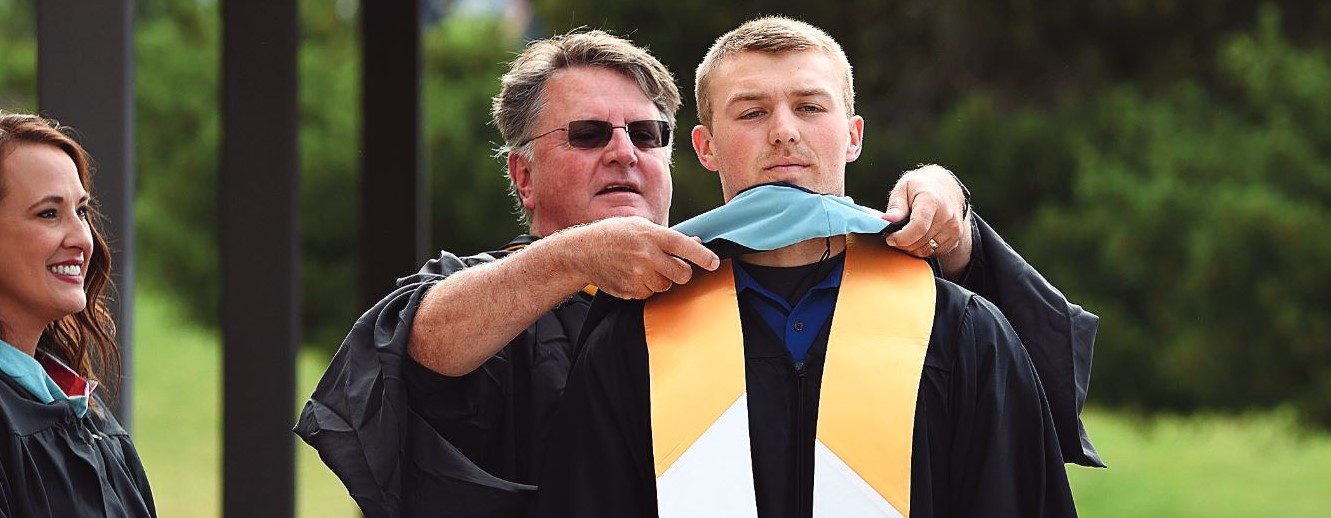 Kolbe Bales, '18, '23, is hooded by College of Education faculty, Dave Dallas, at the 2023 commencement ceremony.