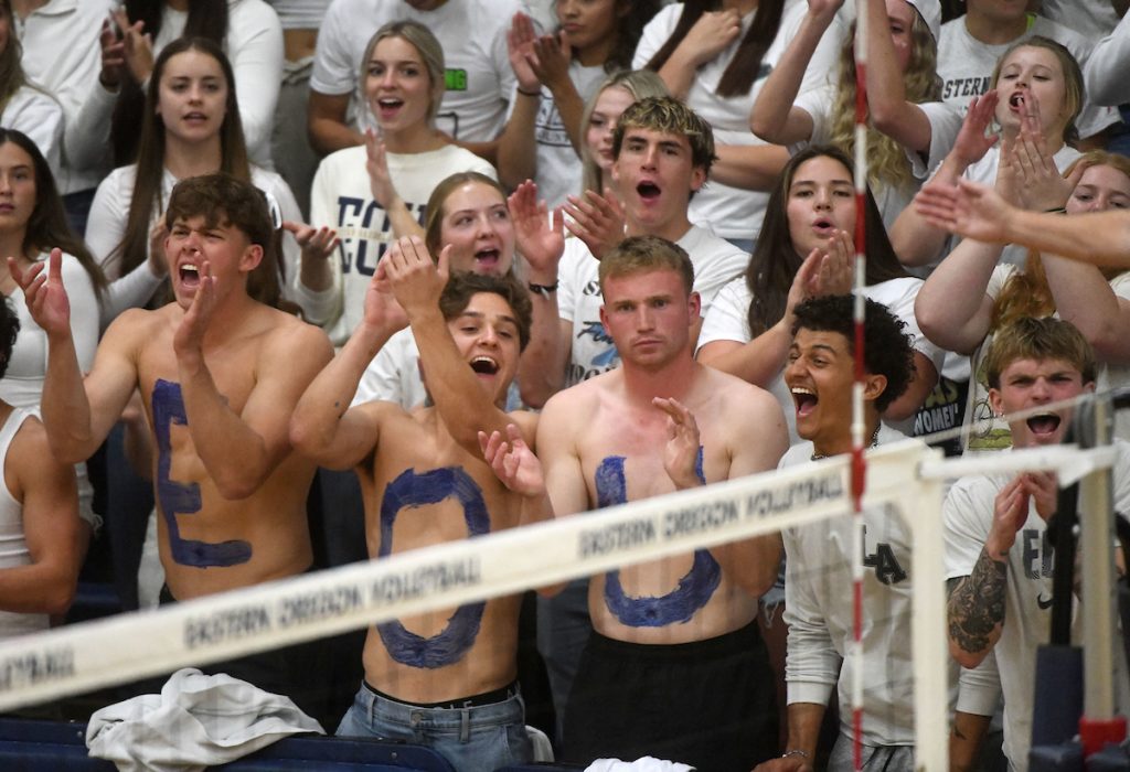 EOU Students cheering at a volleyball game, three male students are shirtless with the letters E O and U on their chests.