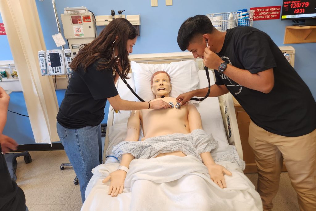 Medquest students holding stethoscopes to manekins