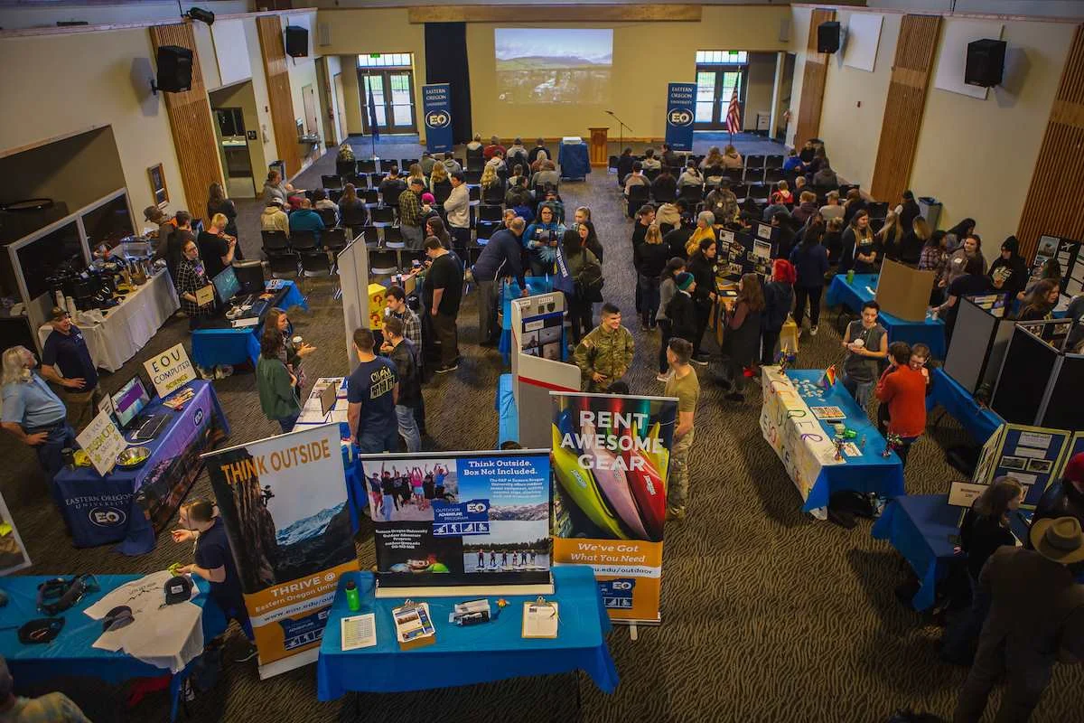 Prospective students and visitors browsing campus information booths and department displays during Eastern Oregon University Preview Day in a large hall.