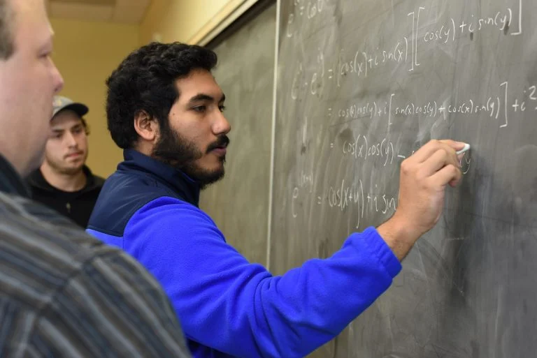 A mathematics student writing on the chalkboard in class.