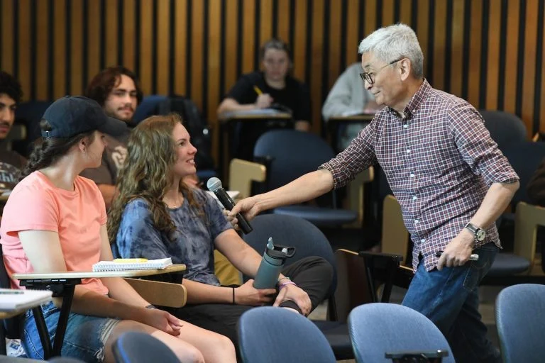 Businessman Bill Imada holding a microphone out to a student in lecture