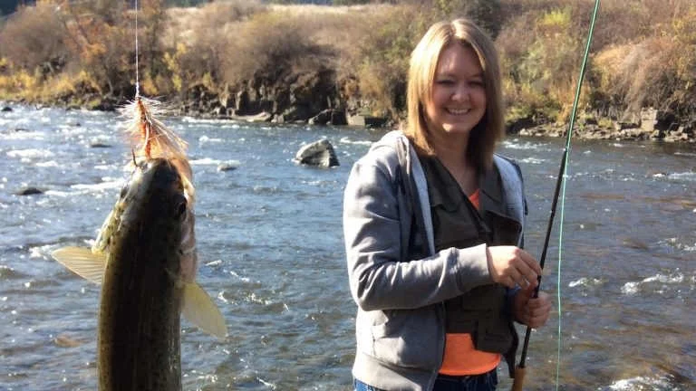 Student holding up a fish they caught in the river they are standing in